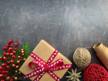 Noel süslemeli kırmızı kurdeleli hediye kutusu ve gri ahşap masada köknar ağacı dalları..