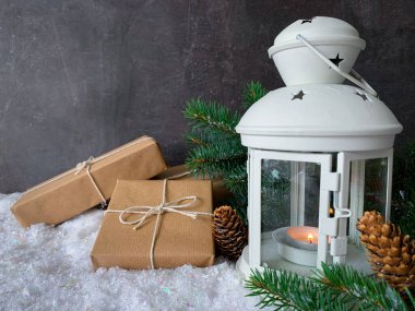 Kahverengi kağıttan hediye kutusu, üzerinde çam dalları ve beyaz fener var..