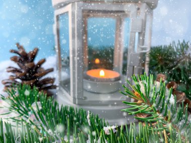 Mum ışığı feneri, köknar ağacı dalları ve mavi arka planda çam kozalakları olan bulanık bir Noel arkaplanı..