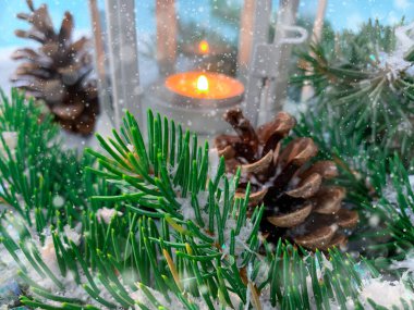 Karlı bir zemin üzerinde kozalaklı çam ağacı dalları ve uzaktan mum lambası. Tatilin bulanık arka plan sihri.