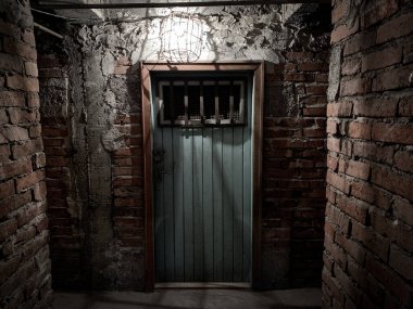 Ahşap paslı zindan kapısının üzerinde parlayan loş ışık.