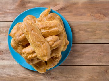 Kahverengi ahşap arka planda mavi bir tabakta Eclairs yığını.