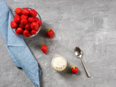 Kasede çilek, çırpılmış krema, çay kaşığı ve gri arka planda keten peçete..