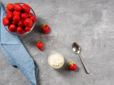 Kasede çilek, çırpılmış krema, çay kaşığı ve gri arka planda keten peçete..