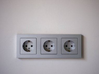 Gri üç modüllü elektrik prizine yakın çekim.