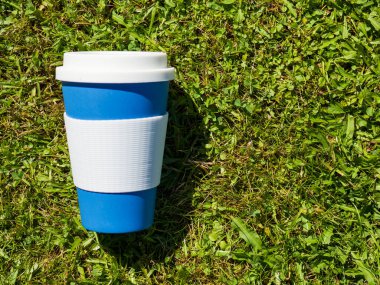 Yeşil çimlerin üzerinde kapağı olan yeniden kullanılabilir bir kahve kupası..