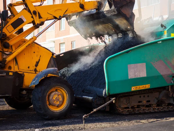 En närbild av en grävmaskinsskopa som lossar färsk het asfalt i en asfaltasfaltasfaltasfalts mottagningstratt. — Stockfoto