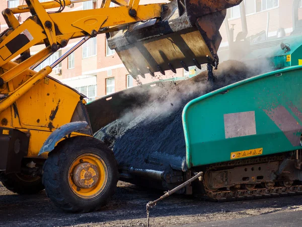 En närbild av en grävmaskinsskopa som lossar färsk het asfalt i en asfaltasfaltasfaltasfalts mottagningstratt. — Stockfoto