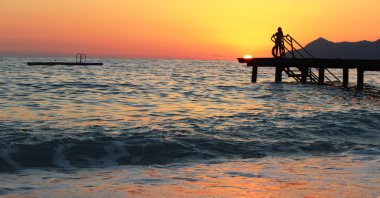 Kız bir iskelede bir gün batımında ayakta