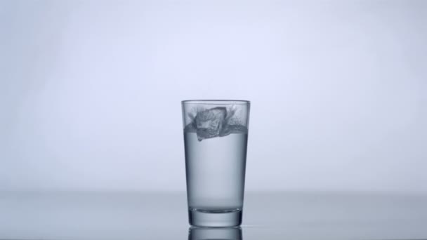 Cubos de hielo cayendo en vidrio con agua — Vídeo de stock