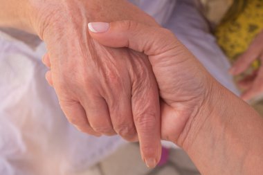 Genç kızın elini dokunur ve kırışık yaşlı bir kadının ellerini tutar.