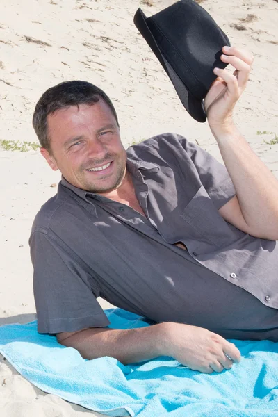 Uomo sulla spiaggia sdraiato nella sabbia cercando di lato sorridente felice — Foto Stock