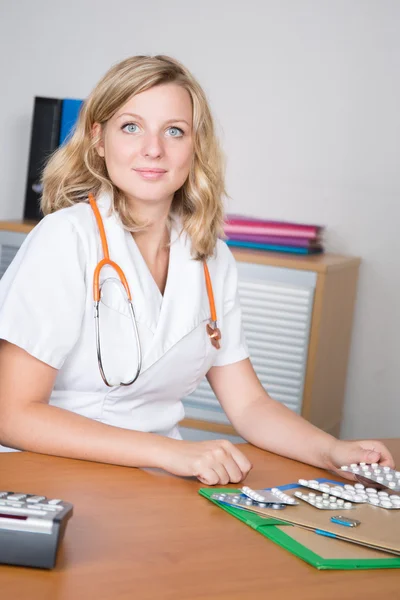 Jonge aantrekkelijke vrouwelijke arts achter balie in kantoor — Stockfoto