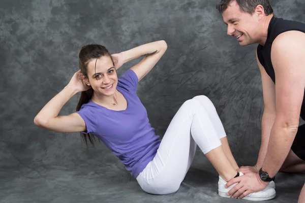 Žena s osobním trenérem dělá sit ups v tělocvičně — Stock fotografie