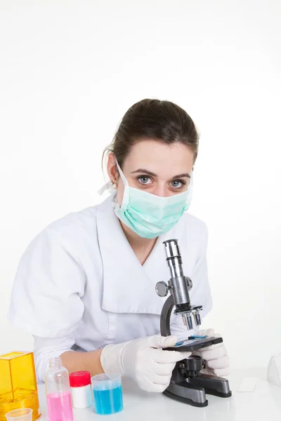 Ένα θηλυκό ιατρική ή επιστημονική ερευνητής ή γιατρό χρησιμοποιώντας το μικροσκόπιο σε εργαστήριο με τον συνάδελφό της Ασίας εκτός εστίασης πίσω της. — Φωτογραφία Αρχείου