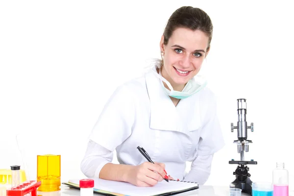 Σοβαρή θηλυκός επιστήμονας χρησιμοποιώντας μικροσκόπιο και γραφής στο μπλόκ σημειώσεων — Φωτογραφία Αρχείου