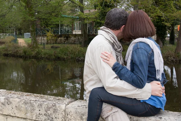 Pareja sentada junto al agua y abrazándose — Foto de Stock