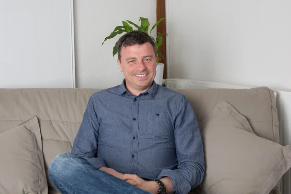 Handsome happy and smiling man at home sitting on the couch — Stock Photo, Image