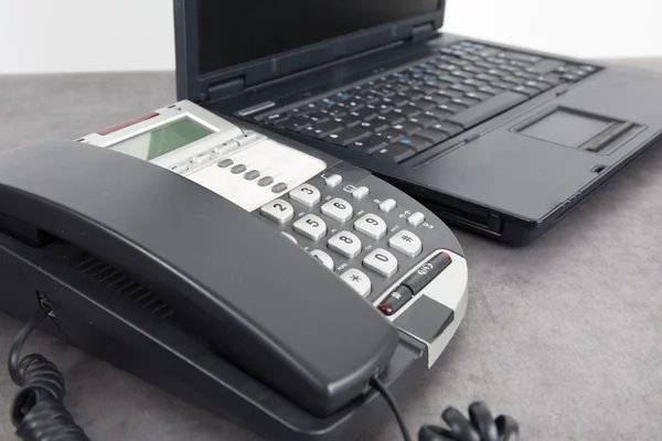 Portátil y teléfono en escritorio gris en una oficina luminosa —  Fotos de Stock