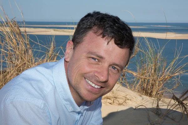 Casual beyaz top parlak plaj arka plan karşı gülümseyen adam — Stok fotoğraf