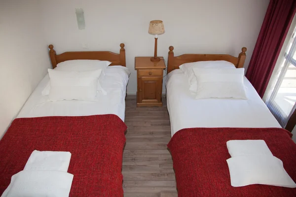 Dos camas rojas dormitorio con mesita de noche y lámpara . — Foto de Stock