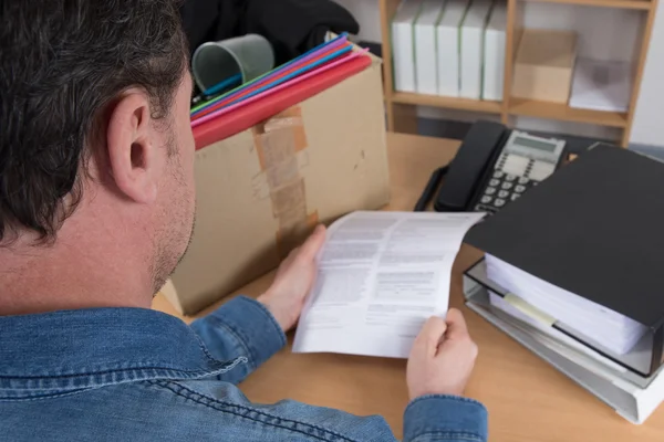 Visão traseira de um homem lendo uma notificação de demissão, preparando sua caixa — Fotografia de Stock