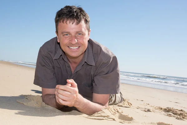 Portret van een aantrekkelijke jongeman liggend op het zand — Stockfoto