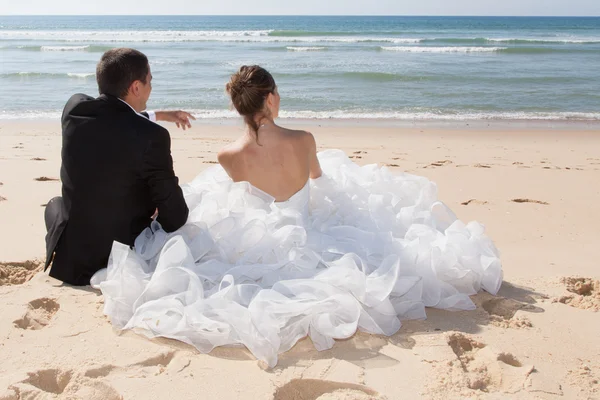 Bride and groom sitting on the beach — Stock Photo, Image