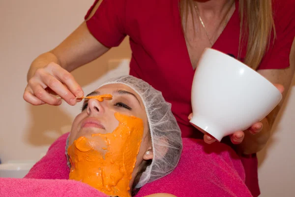 Frau mit Tongesichtsmaske von Kosmetikerin auftragen lassen. — Stockfoto