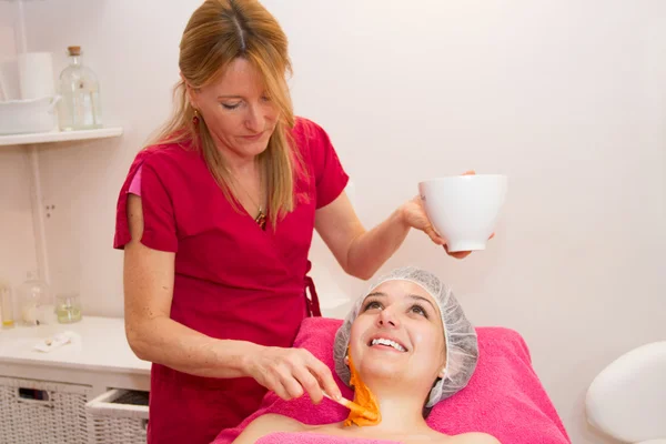 Frau mit Ton Gesichtsmaske Anwendung durch weibliche Kosmetikerin. — Stockfoto