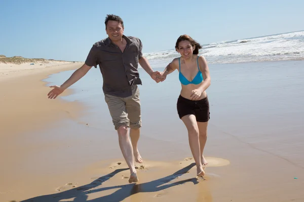 Happy couple walking on beach smiling holding around each other. — Stock Photo, Image