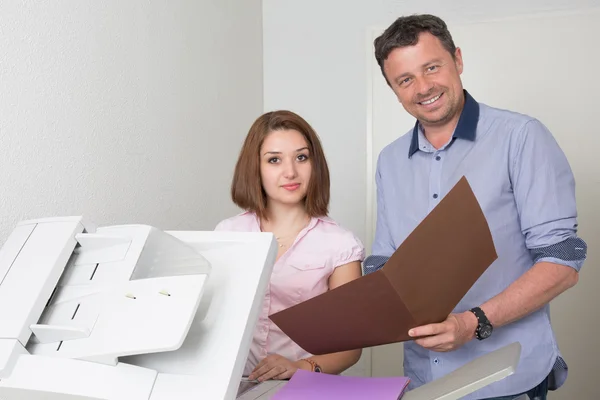 Empresário e mulher usando uma máquina de cópia sorrindo — Fotografia de Stock