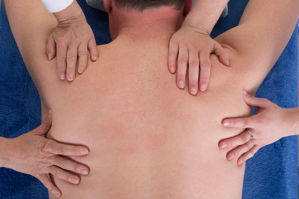 Vier Hände auf dem Rücken eines Mannes für eine Massage — Stockfoto