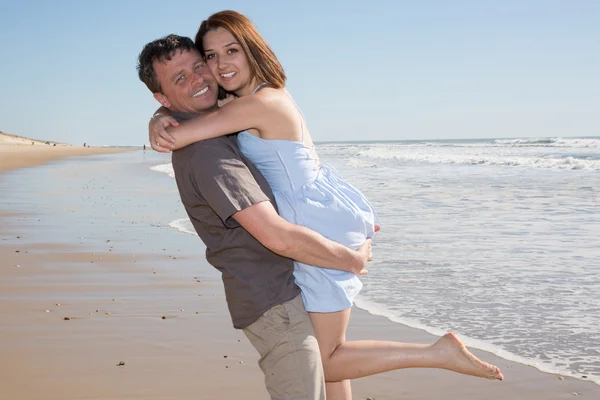 Мужчина держит женщину на руках на пляже улыбаясь — стоковое фото