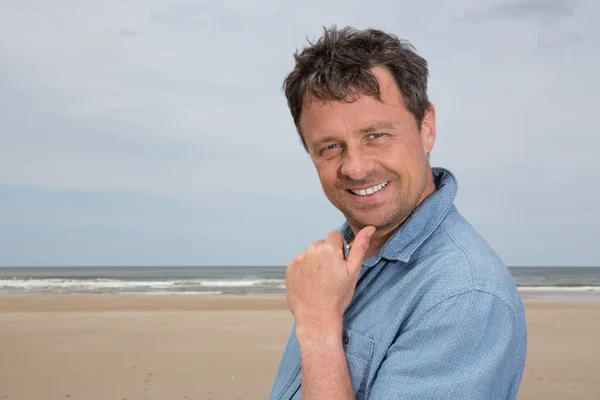 Uomo di mezza età in piedi sulla spiaggia sorridente sotto il cielo blu — Foto Stock