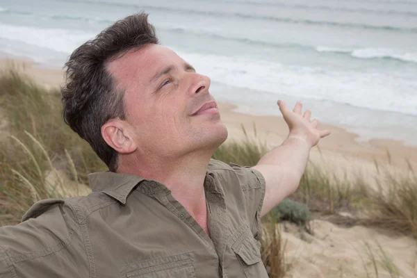 Счастливый человек дышит глубоко с поднятыми руками на пляже — стоковое фото