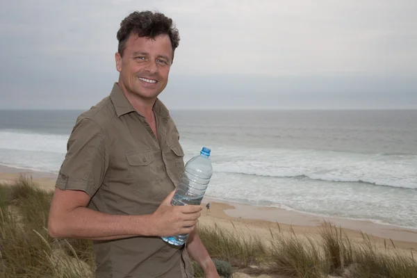 Uomo caucasico in posa sulla spiaggia - con una bottiglia d'acqua in mano — Foto Stock