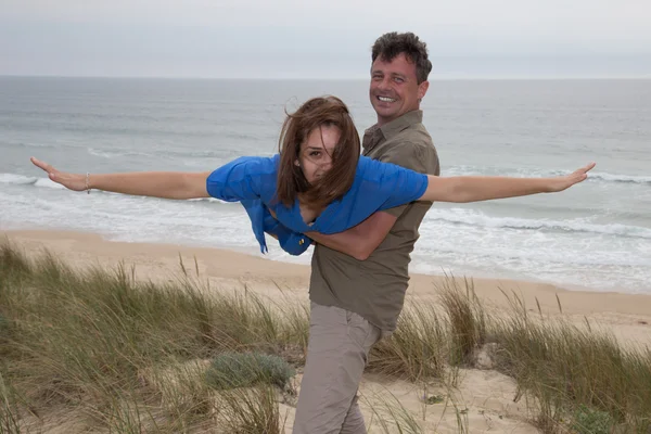 Schöner Mann hält Frau am Strand wie Flugzeug frei — Stockfoto