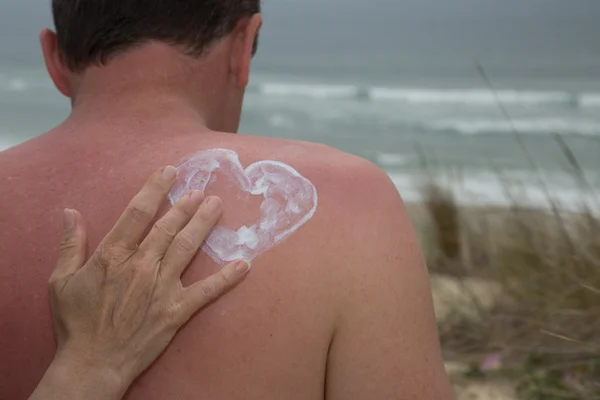 Hands putting sun proctection shaping a heart on man's back — Stock Photo, Image