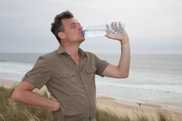 Kaukasische man die zich voordeed op het strand - goed drinkwater voor gezondheid — Stockfoto