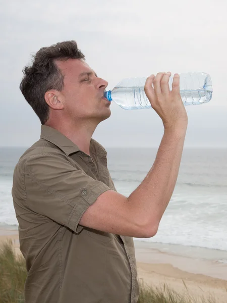Caucasian man posing at the beach - drinking water