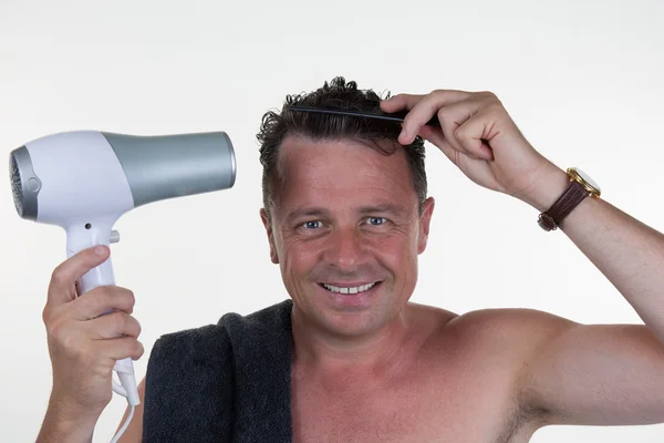 Atractivo hombre sonriente usando secador de pelo y peine en el baño —  Fotos de Stock