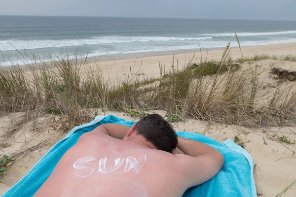 Człowiek z powrotem lotionthe opalenizny na plaży napisane słońce — Zdjęcie stockowe