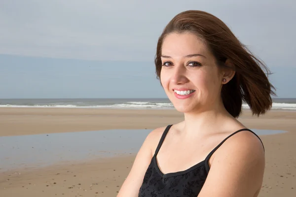 Sonriente chica morena en vestido negro posando en la playa durante la puesta del sol . —  Fotos de Stock