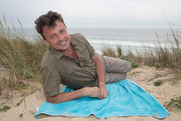 Uomo allegro sulla spiaggia sdraiato nella sabbia godendo — Foto Stock