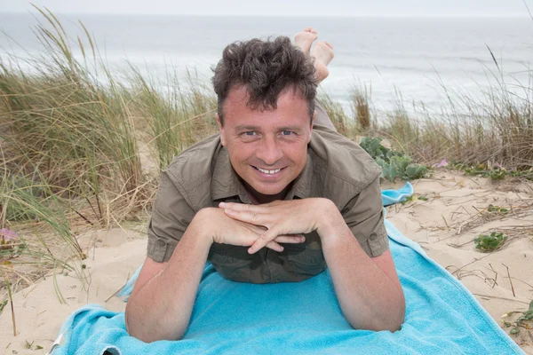 Man on beach lying in sand looking to camera enjoying — Stock Photo, Image