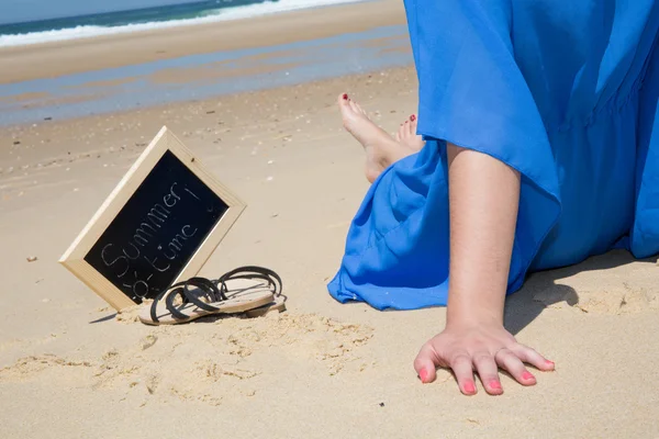 Las manos y la pierna de la mujer con pizarra y la hora de verano en ella contra el mar — Foto de Stock