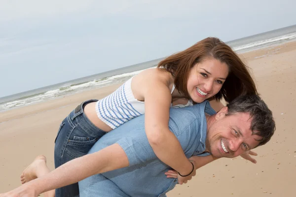 Happy couple laughing together at the beach piggy back