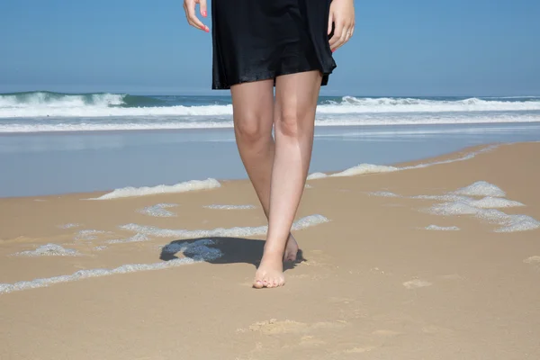Vrouw in een zwarte jurk, lopen op zand — Stockfoto