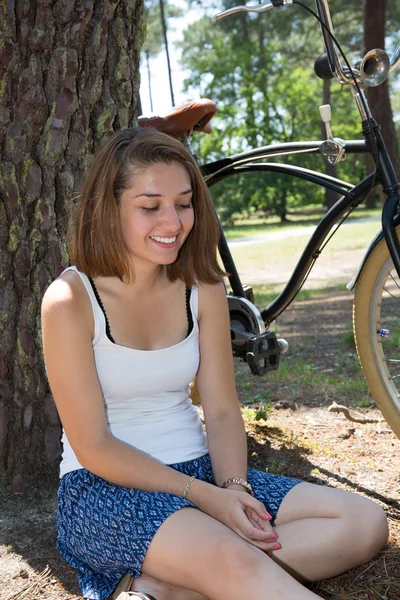 Szép fiatal lány ül egy fa-val blackbicycle - szabadban — Stock Fotó